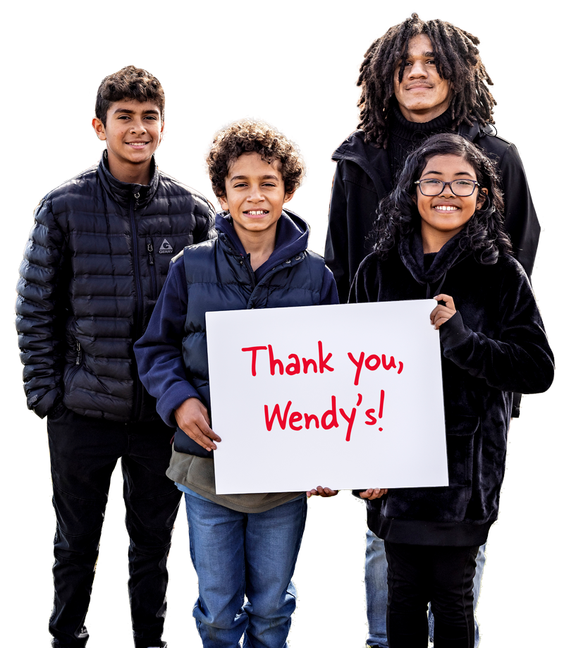 Four smiling kids stand together, celebrating a partnership. One boy in front holds a white sign with red text that reads, Thank you, Wendy’s! The background is plain white.